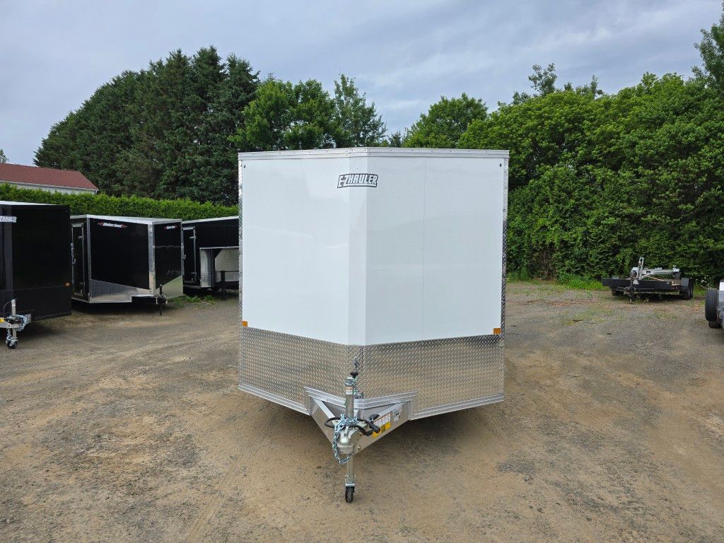 Une remorque blanche est garée sur un terrain en terre.