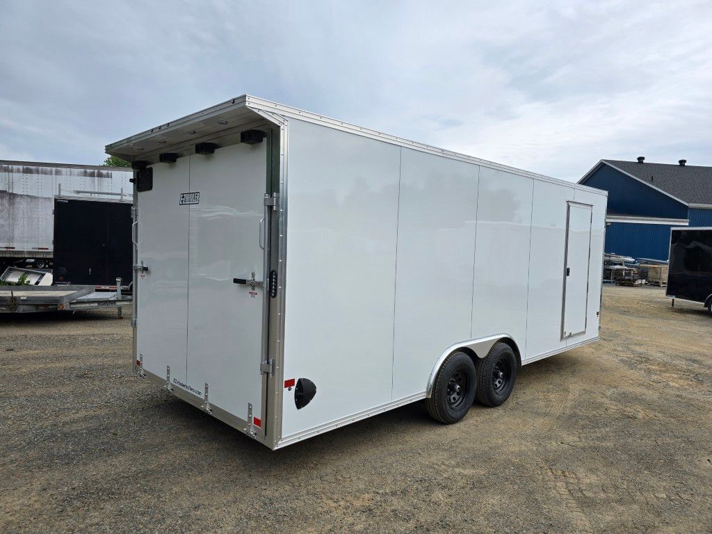 Une remorque blanche est garée sur un terrain en gravier devant un bâtiment.