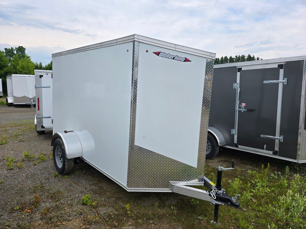 Une remorque blanche est garée sur un terrain en gravier à côté d'une remorque noire.