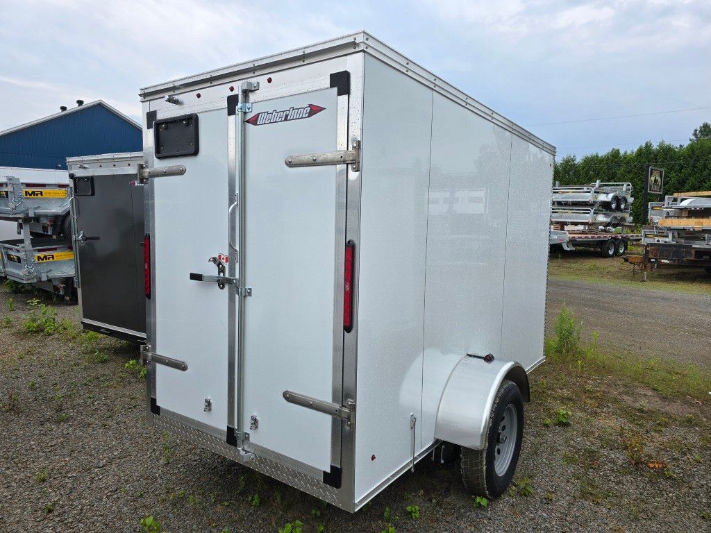 Une remorque blanche est garée sur un terrain en gravier.