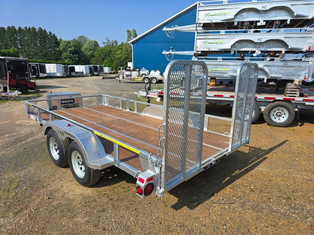 Remorque utilitaire argentée avec pont en bois, rails de sécurité et boîte à outils garée à l'extérieur.