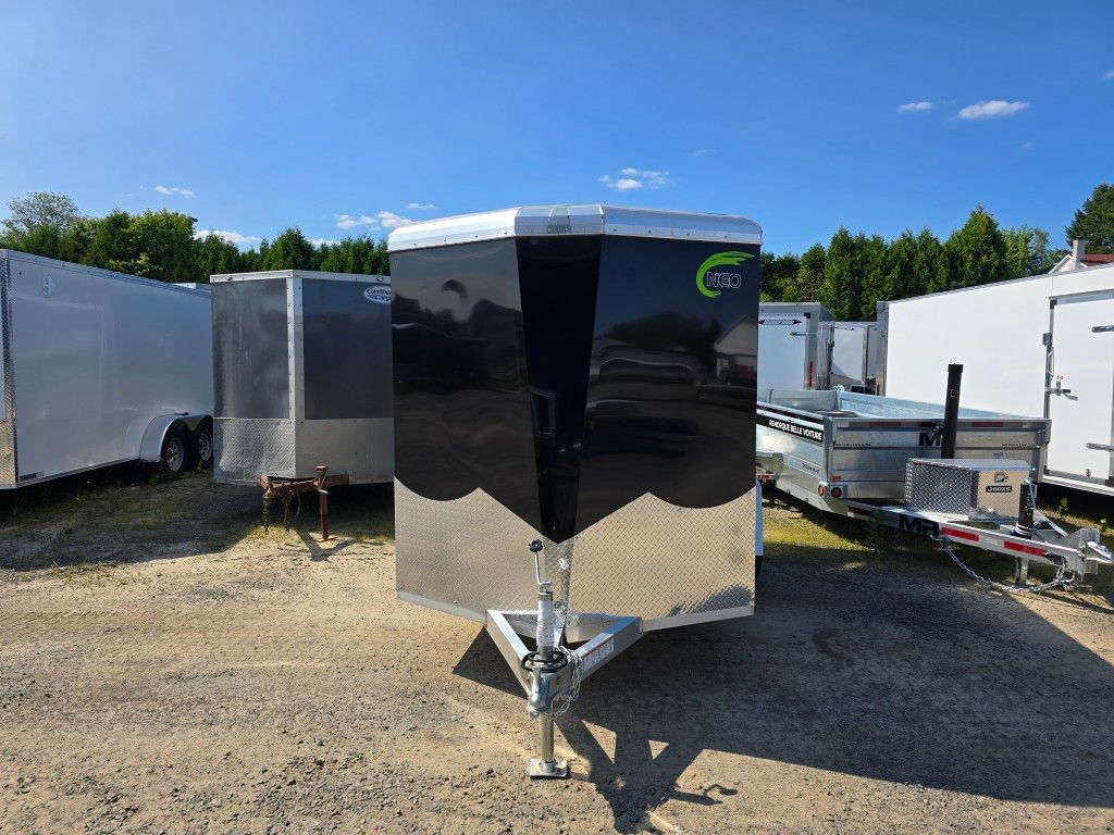 Remorque cargo fermée noire et argentée sur un terrain en gravier sous un ciel bleu.