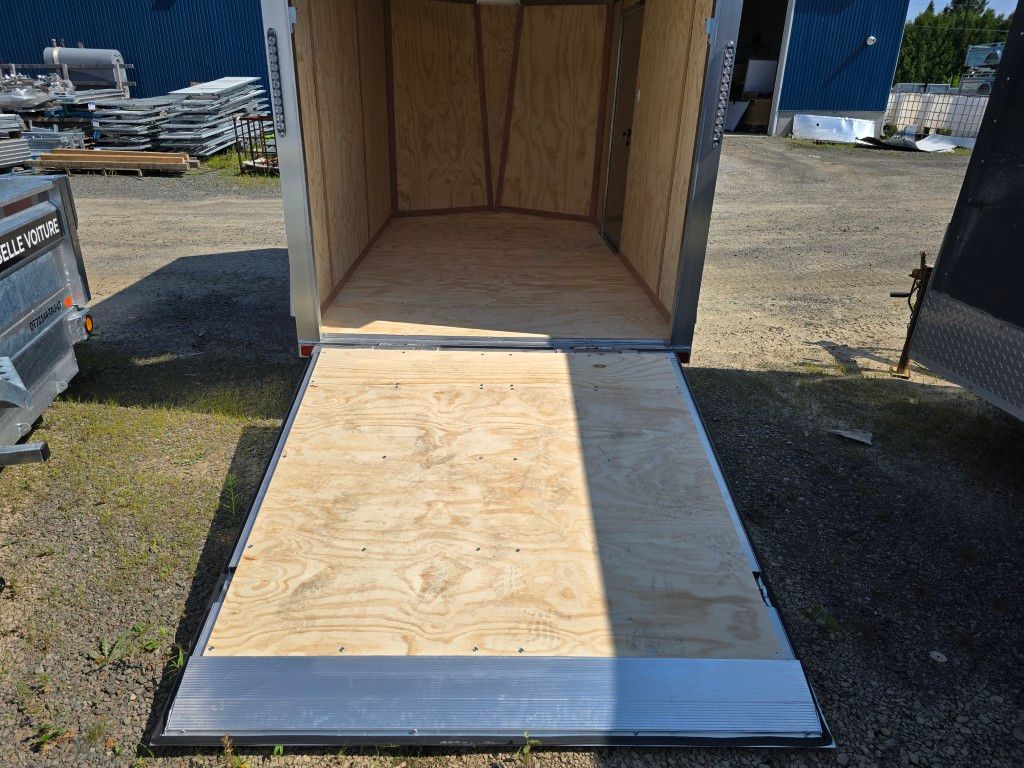 Remorque cargo ouverte avec rampe en bois, garée à l'extérieur sur du gravier.