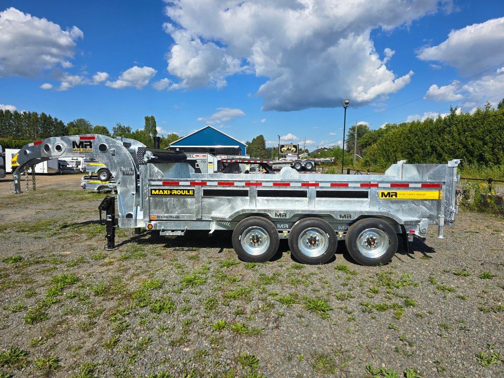 Remorque à benne basculante argentée sur l'herbe, ciel bleu et un bâtiment en arrière-plan.