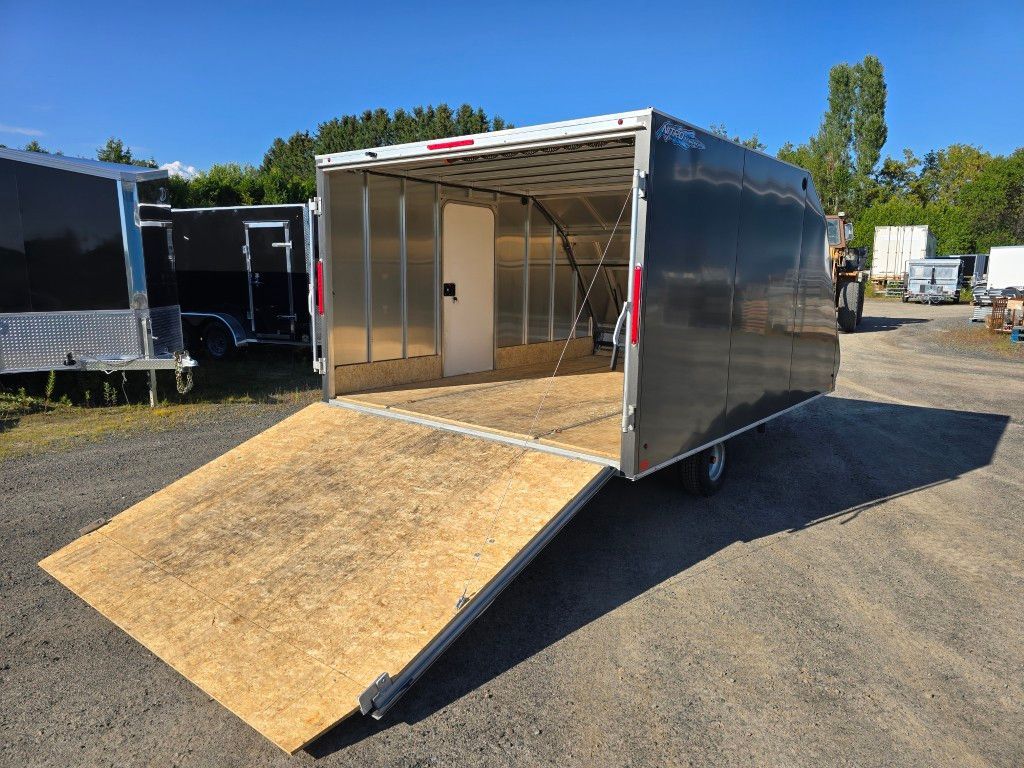 Remorque fermée noire avec rampe ouverte sur terrain en gravier.