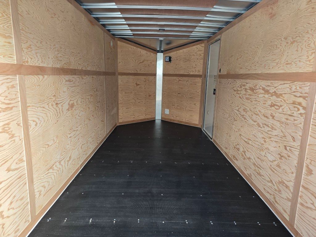 Intérieur de remorque fermée vide avec parois en bois, plancher noir et supports métalliques.