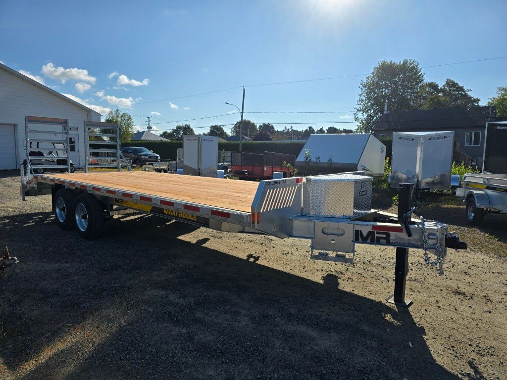 Une remorque à plateau avec plancher en bois, garée à l'extérieur. Ciel bleu éclatant, autres remorques en arrière-plan.