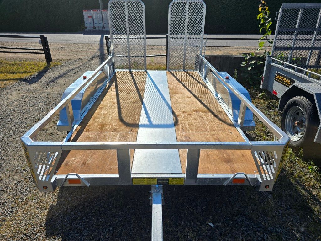 Deux remorques utilitaires stationnées sur du gravier, l'une avec des côtés en aluminium et une rampe, l'autre avec des côtés en métal.