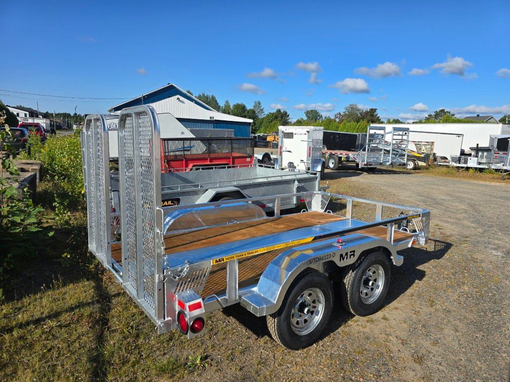 Remorque utilitaire argentée avec côtés grillagés et rampe, deux roues, stationnée à l'extérieur par une journée ensoleillée.