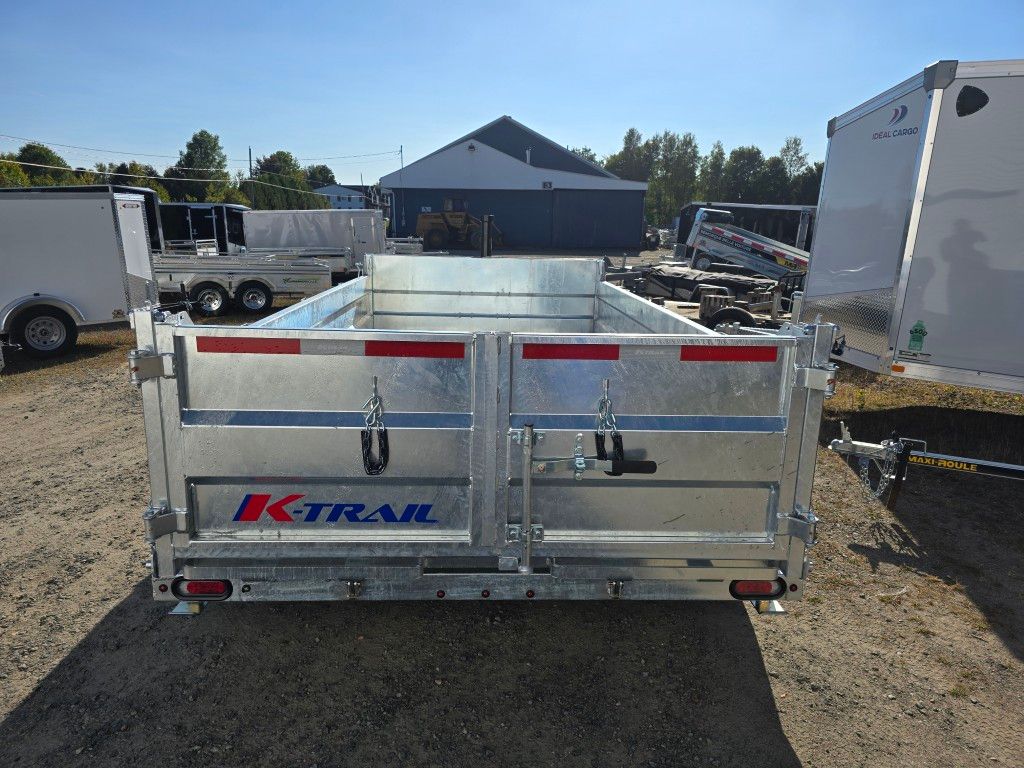 Une remorque à benne basculante K-Trail argentée avec deux portes arrière sur un terrain par une journée ensoleillée.