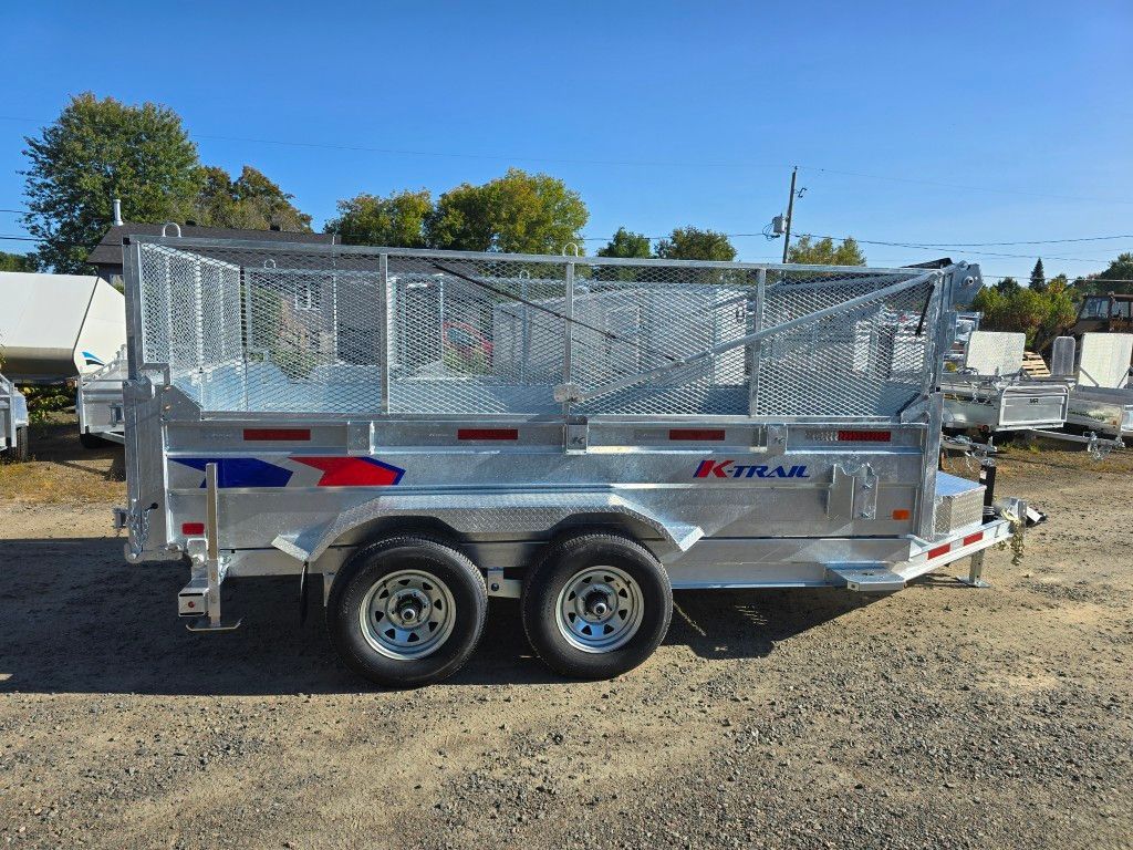 Remorque à benne basculante argentée avec roues jumelées, côtés en treillis métallique, stationnée à l'extérieur sur du gravier.