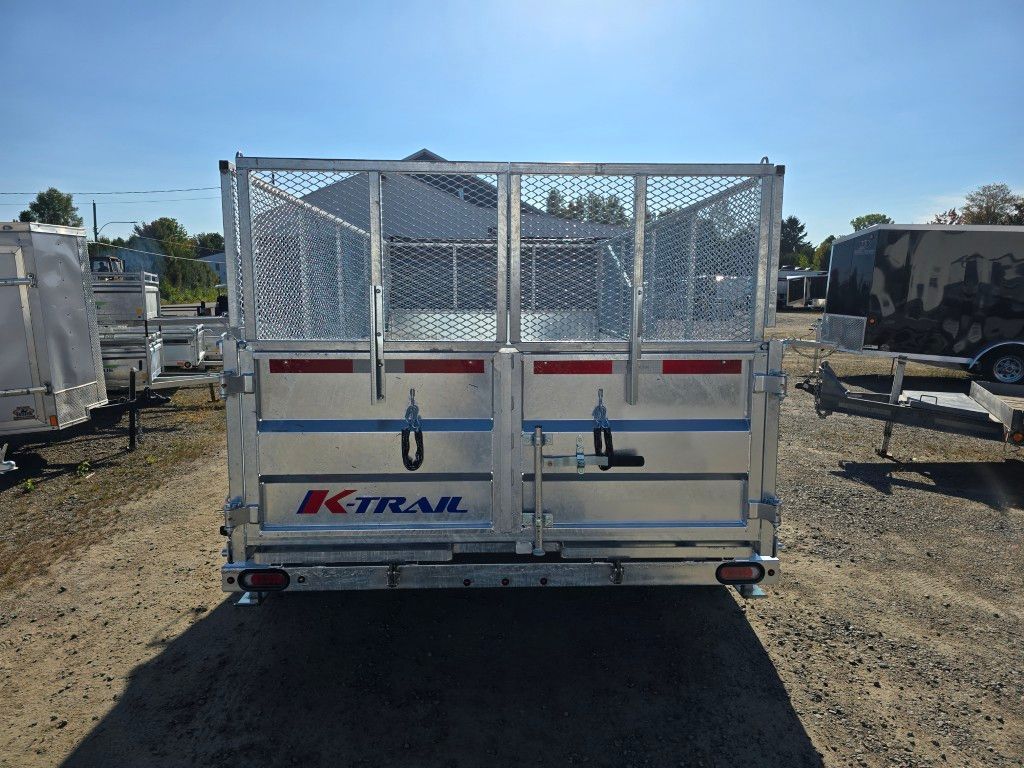 Vue arrière d'une remorque K-TRAK argentée avec une cage grillagée, dans un cadre extérieur.