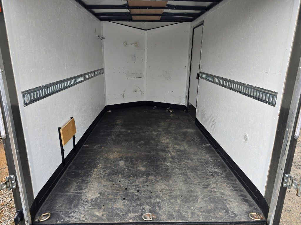 Intérieur d'une remorque cargo vide. Parois blanches, plancher noir et rails d'arrimage.