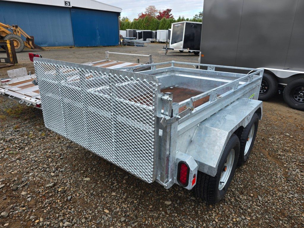 Remorque utilitaire argentée avec côtés grillagés et plancher en bois, stationnée sur gravier.