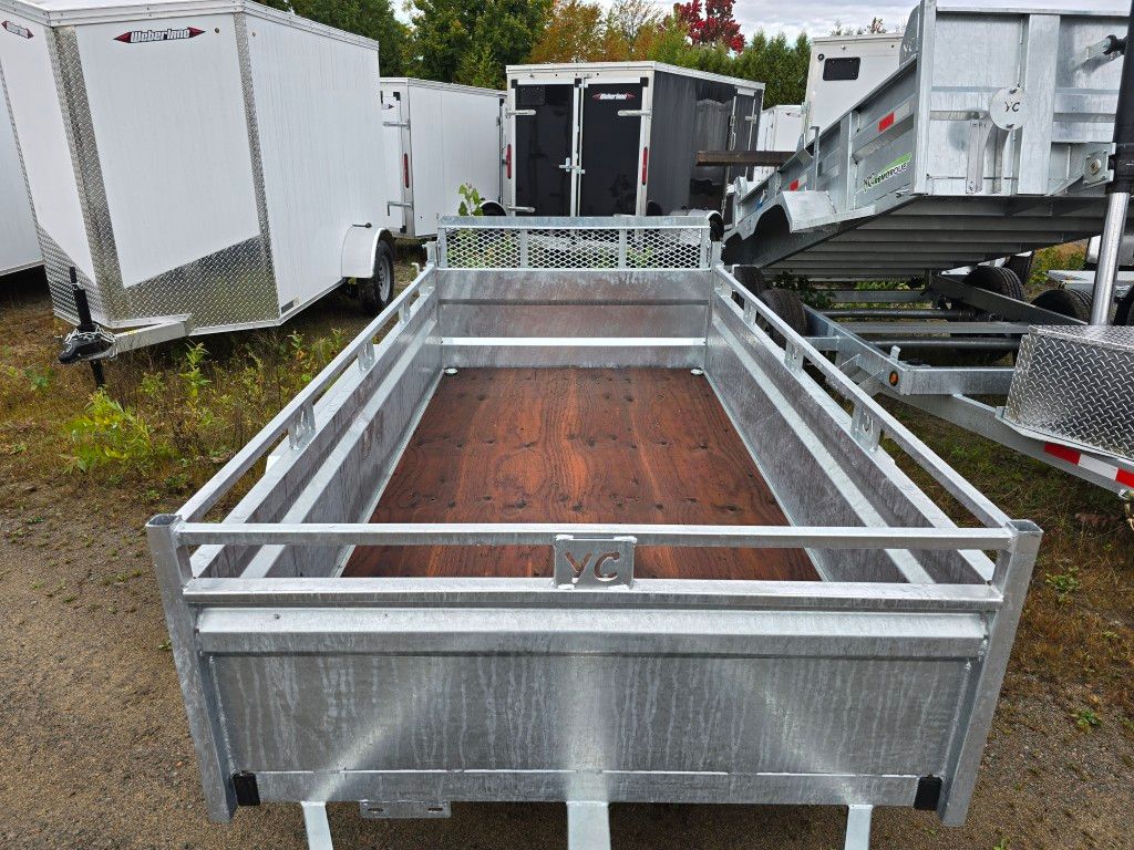 Une remorque utilitaire en métal avec plancher en bois et garde-corps. Remorques en arrière-plan.