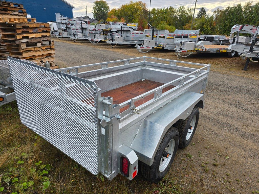 Remorque utilitaire argentée avec côtés grillagés et plancher en bois, stationnée à l'extérieur.