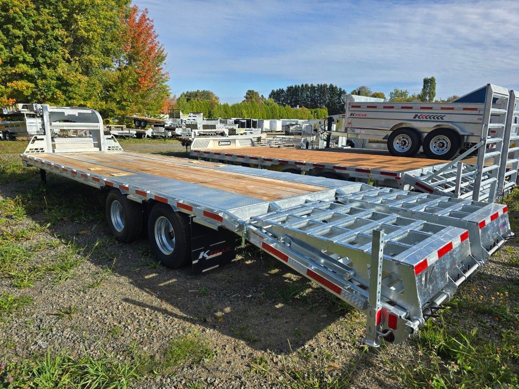 Remorque à plateau avec châssis en aluminium, plateau en bois et remorque à bétail partiellement visible dans un champ.