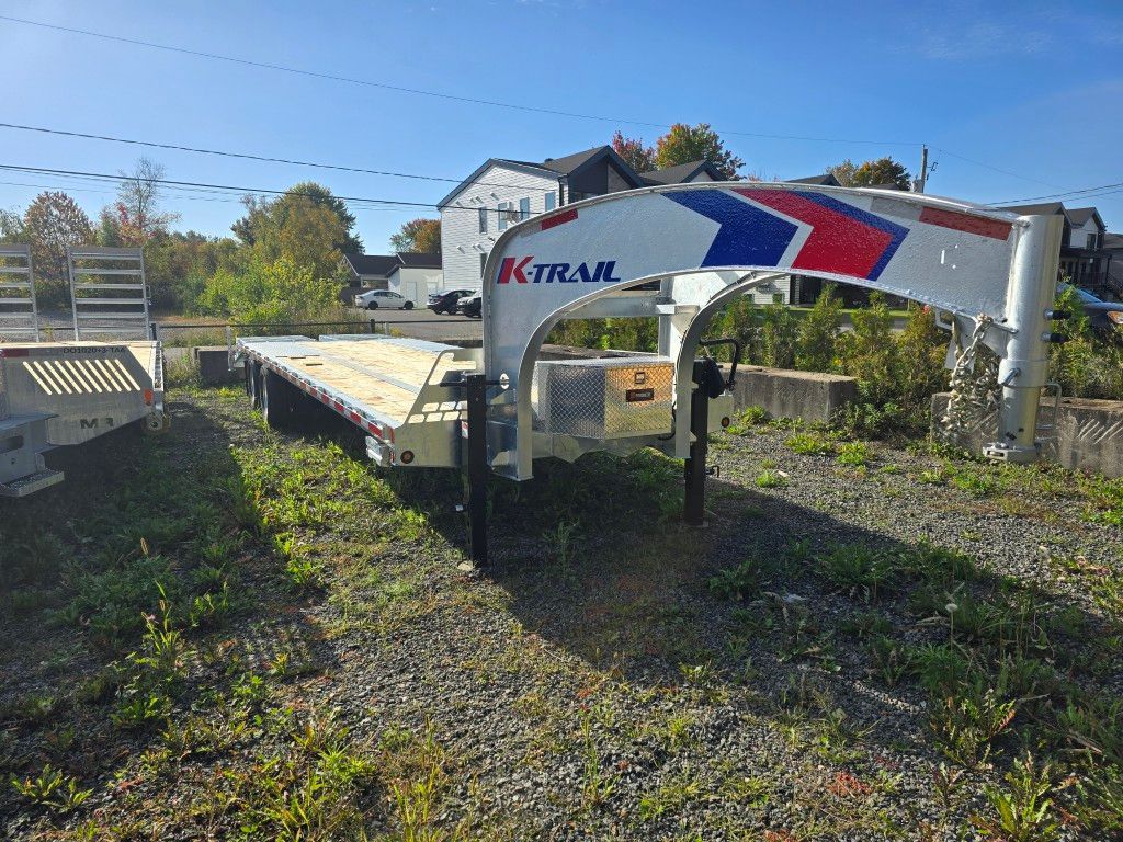 Une remorque à plateau X-Trail garée sur un terrain de gravier et d'herbe par une journée ensoleillée.