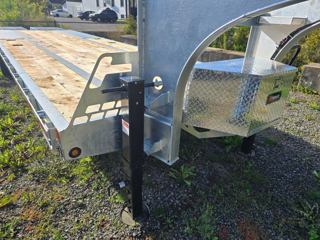 Une remorque à plateau en acier galvanisé avec une boîte à outils en tôle diamantée et un cric noir sur de l'herbe verte.