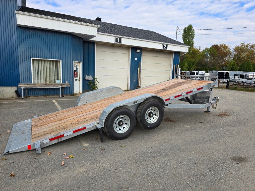 Remorque à plateau stationnée sur l'asphalte devant un bâtiment bleu avec portes de garage.