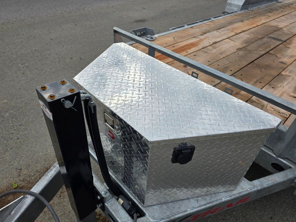 Coffre à outils en aluminium plaqué diamant monté sur une remorque; dessus incliné, poignée noire, stationné sur le trottoir.