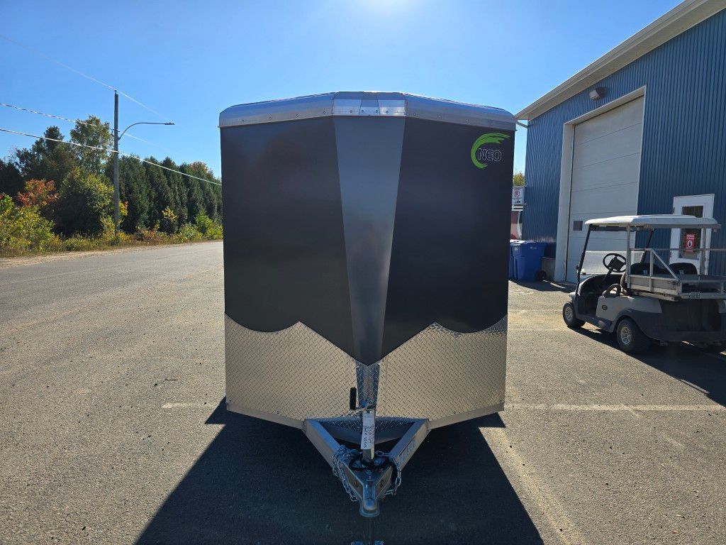 Remorque fermée noire et argentée garée sur le trottoir, sous un ciel bleu, avec une voiturette de golf à proximité.