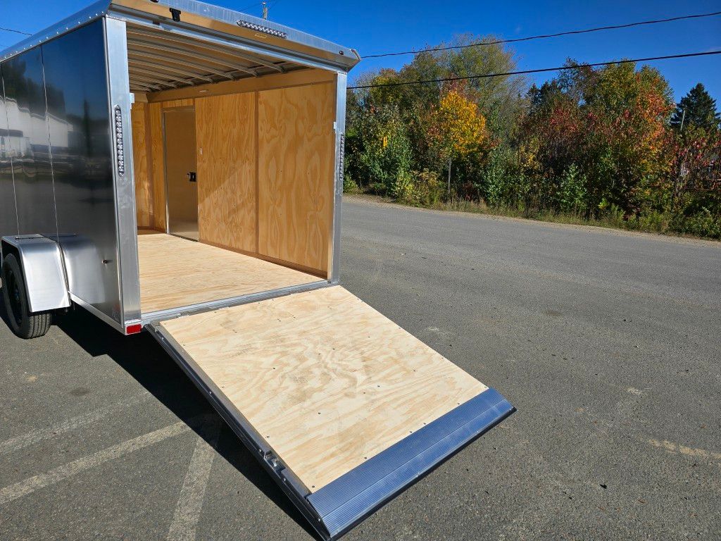 Remorque cargo avec rampe d'accès, garée sur asphalte. Intérieur boisé, feuillage d'automne en arrière-plan.