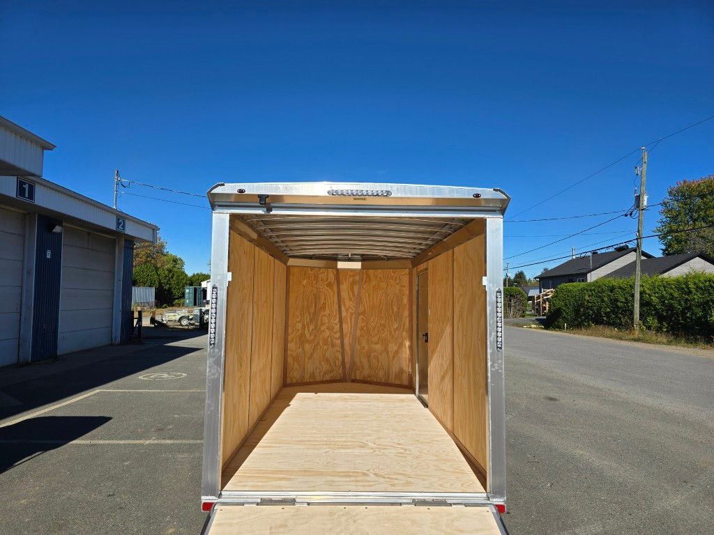 Remorque cargo vide, intérieur en bois, garée sur une route pavée, ciel bleu vif.