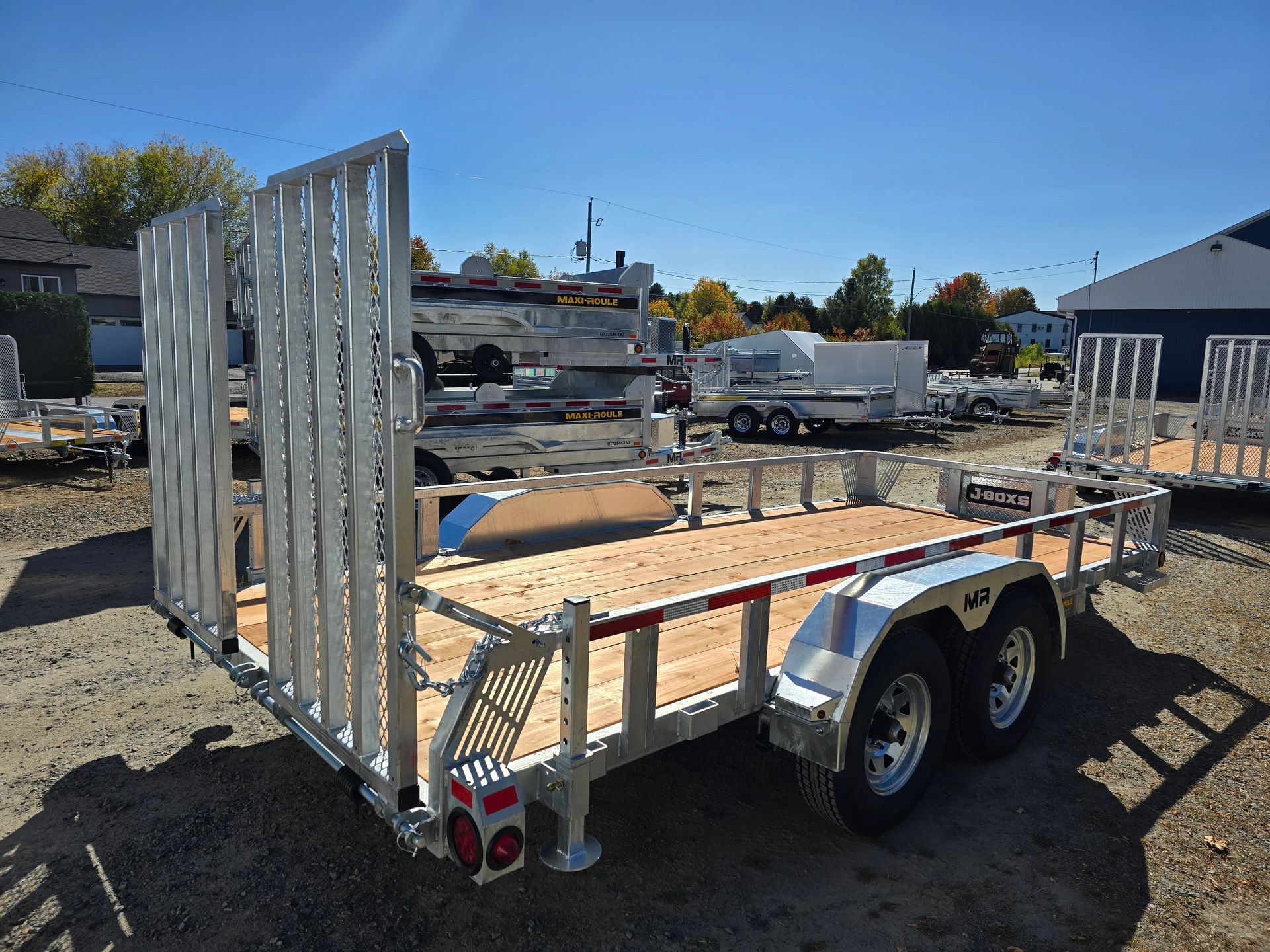 Remorque utilitaire en aluminium avec pont en bois et rails latéraux, stationnée à l'extérieur par une journée ensoleillée.