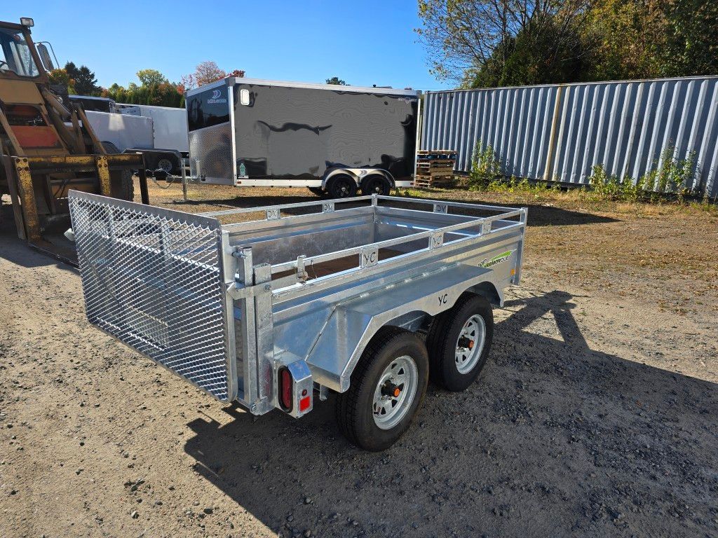 Remorque utilitaire argentée avec panneaux latéraux en filet et deux roues, stationnée sur du gravier à l'extérieur.