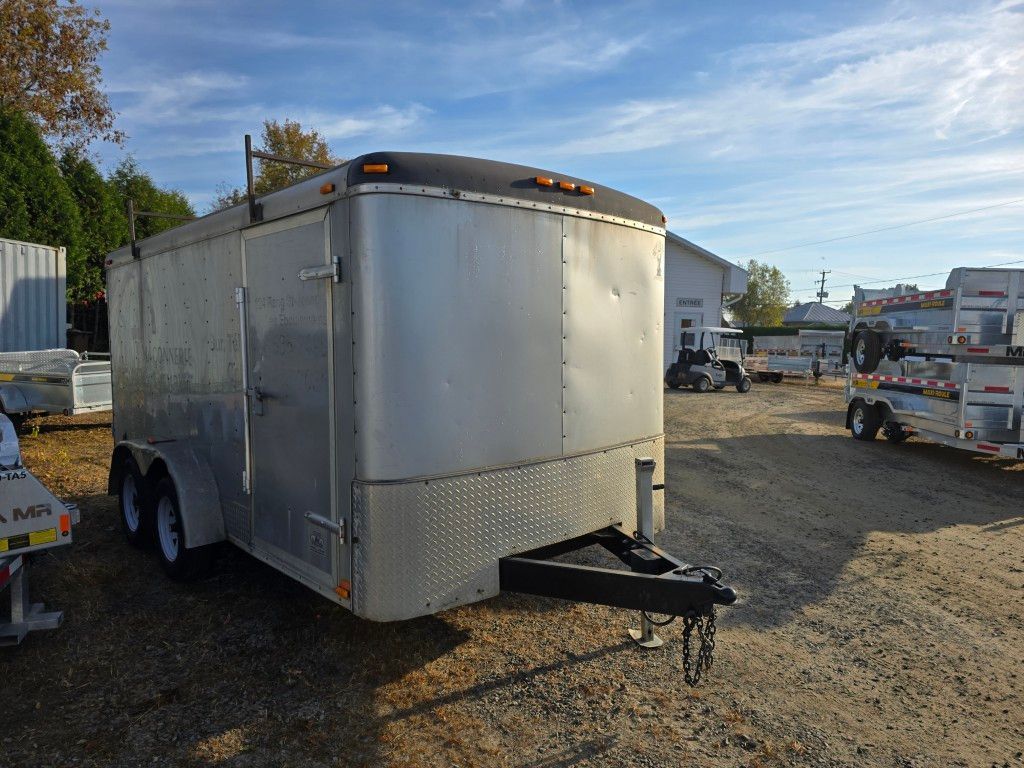Remorque fermée argentée avec garniture et attelage noirs, garée à l'extérieur sur du gravier.