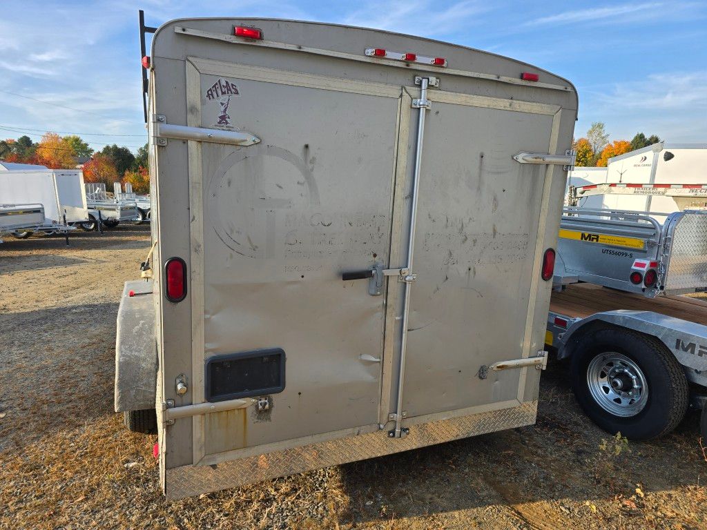 Vue arrière d'une remorque fermée beige avec portes fermées, dans un cadre extérieur.