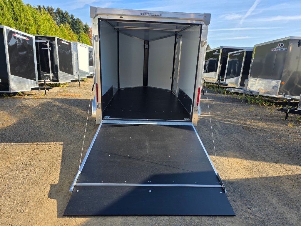 Une remorque cargo ouverte et vide, avec une rampe d'accès. Noir et argent, sur fond de terrain vague.