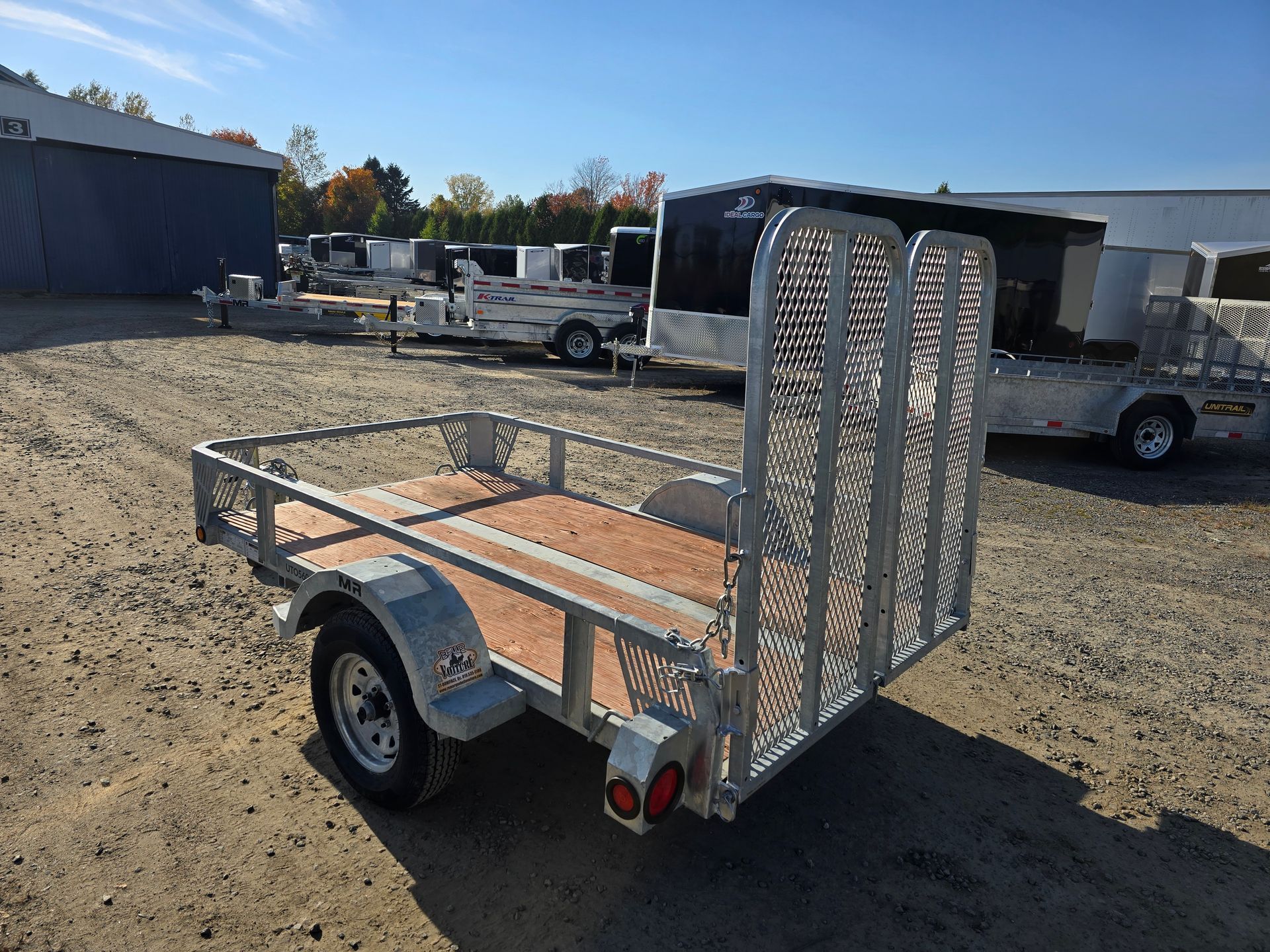 Une petite remorque utilitaire ouverte avec une rampe, garée à l'extérieur par une journée ensoleillée.