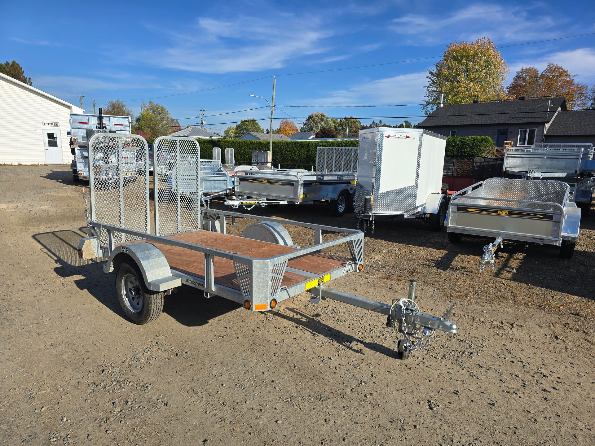 Plusieurs remorques utilitaires de différentes tailles sont stationnées à l'extérieur sur un terrain gravillonné.