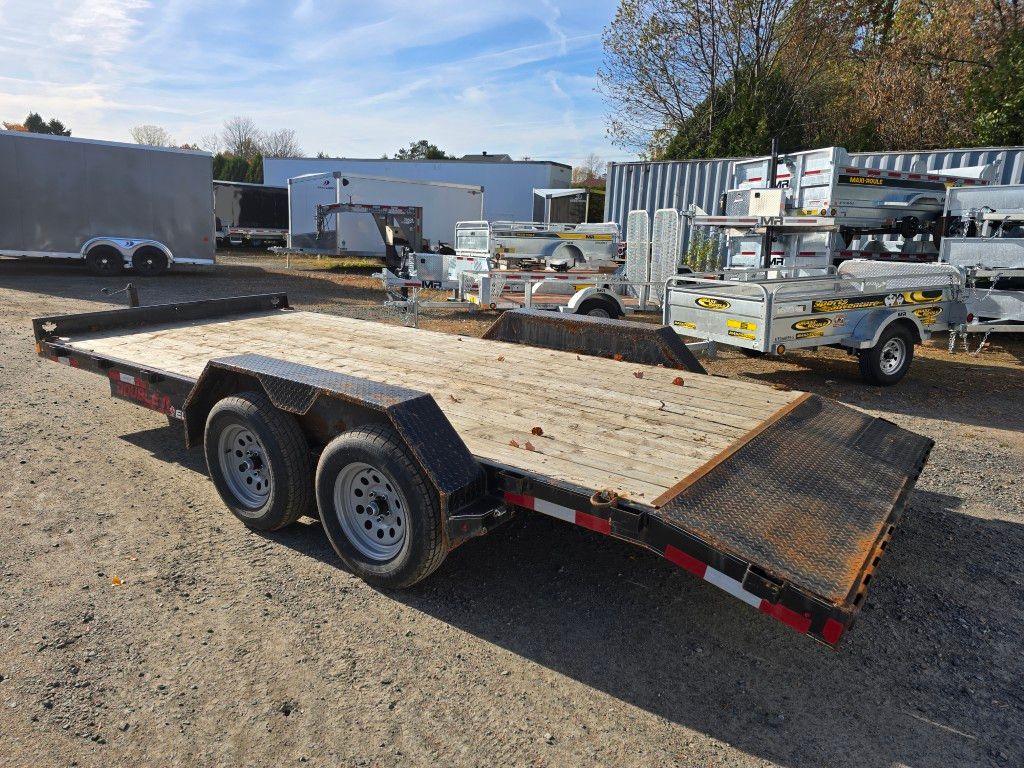 Remorque plateau à roues jumelées, stationnée sur un terrain extérieur avec d'autres remorques.