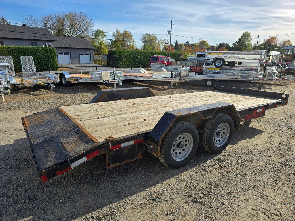 Remorque plateau à deux essieux et plancher en bois, stationnée sur du gravier.