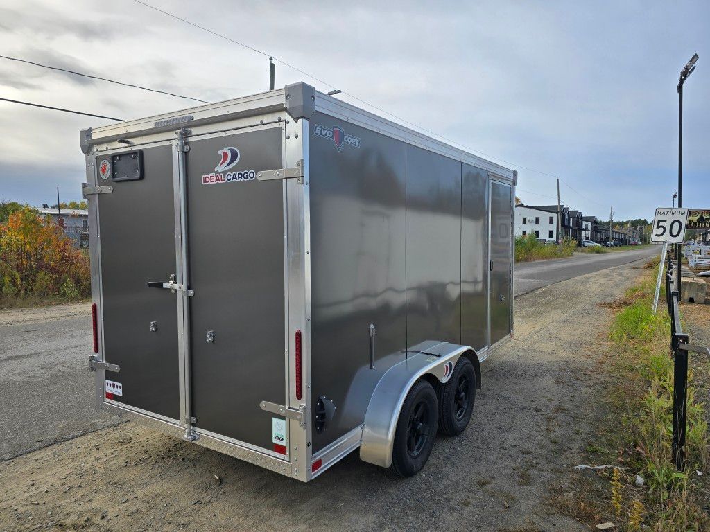 Remorque fermée grise stationnée sur une route, avec deux pneus noirs.