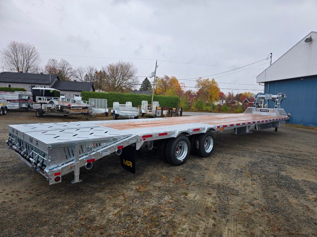 Remorque plateau stationnée sur du gravier, métal gris avec roues, journée nuageuse.