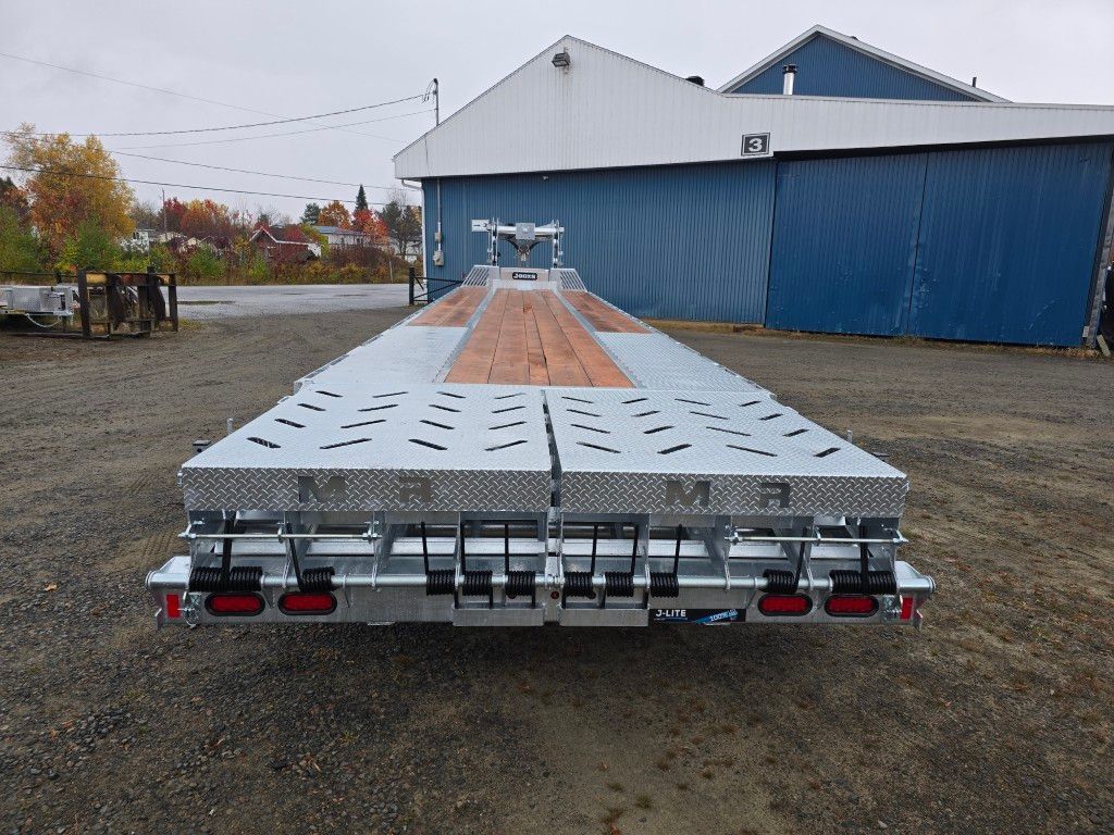 Remorque plateau neuve et vide sur un terrain gravillonné, avec un bâtiment en arrière-plan.