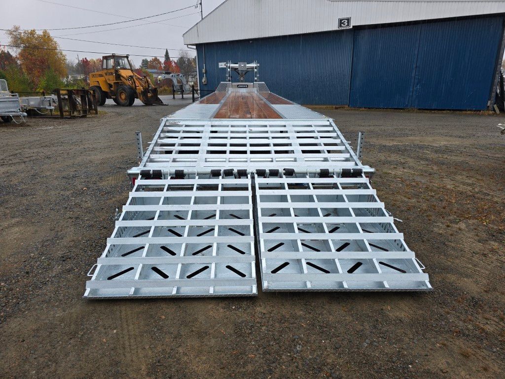 Une remorque à bétail en métal avec rampes ouvertes, stationnée à l'extérieur.