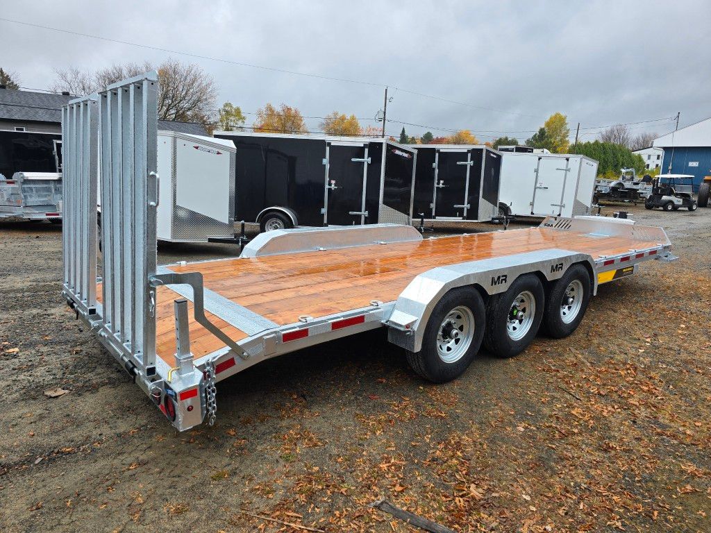 Une grande remorque argentée à plancher en bois et à trois essieux est garée dehors par temps couvert.
