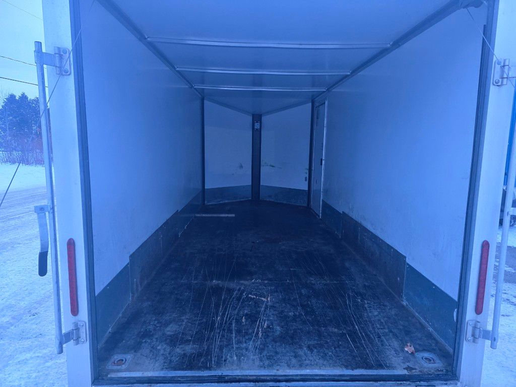 Intérieur d'une remorque blanche vide, ouverte à l'arrière, avec un sol sombre.