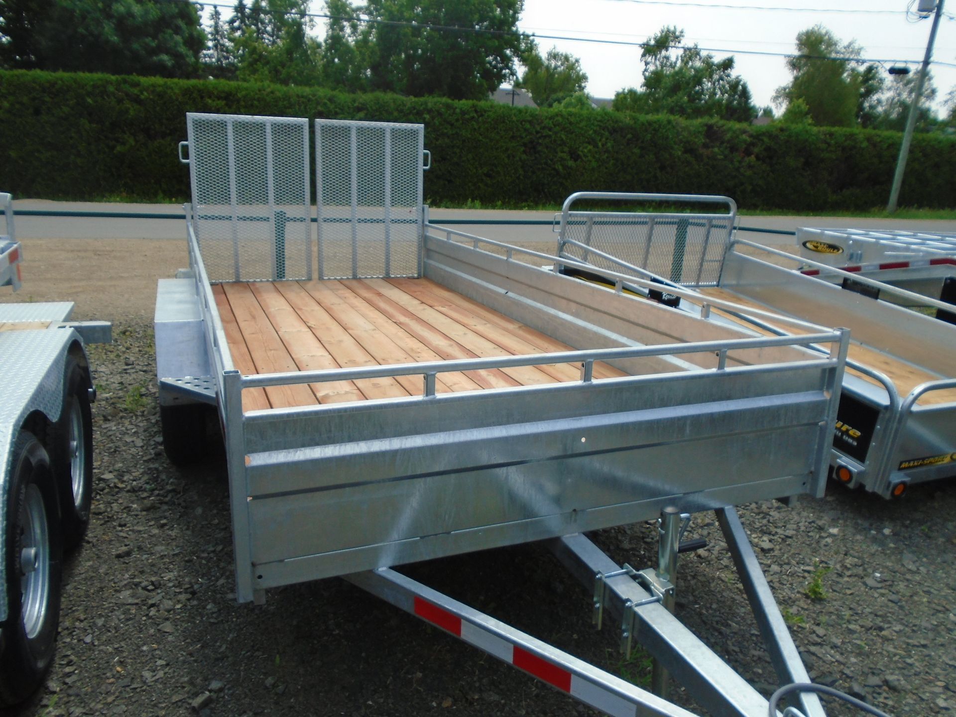 Remorque utilitaire en aluminium avec plancher en bois, cage métallique à l'avant, stationnée à l'extérieur.