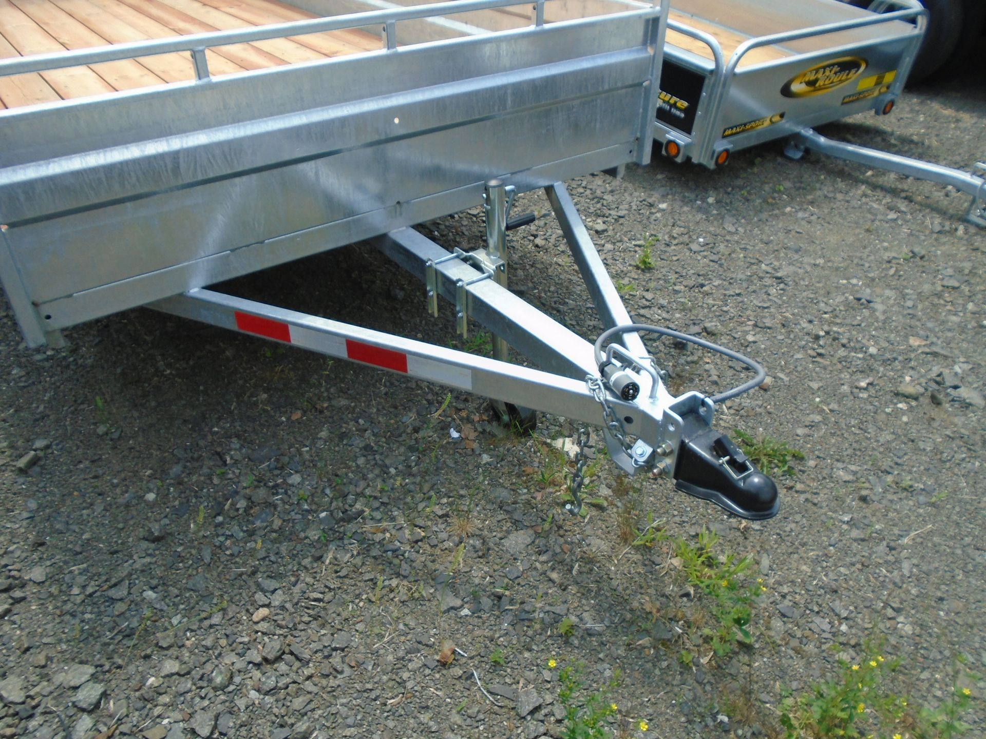 Attelage de remorque sur une remorque grise et argent avec un pont en bois; posé sur du gravier.