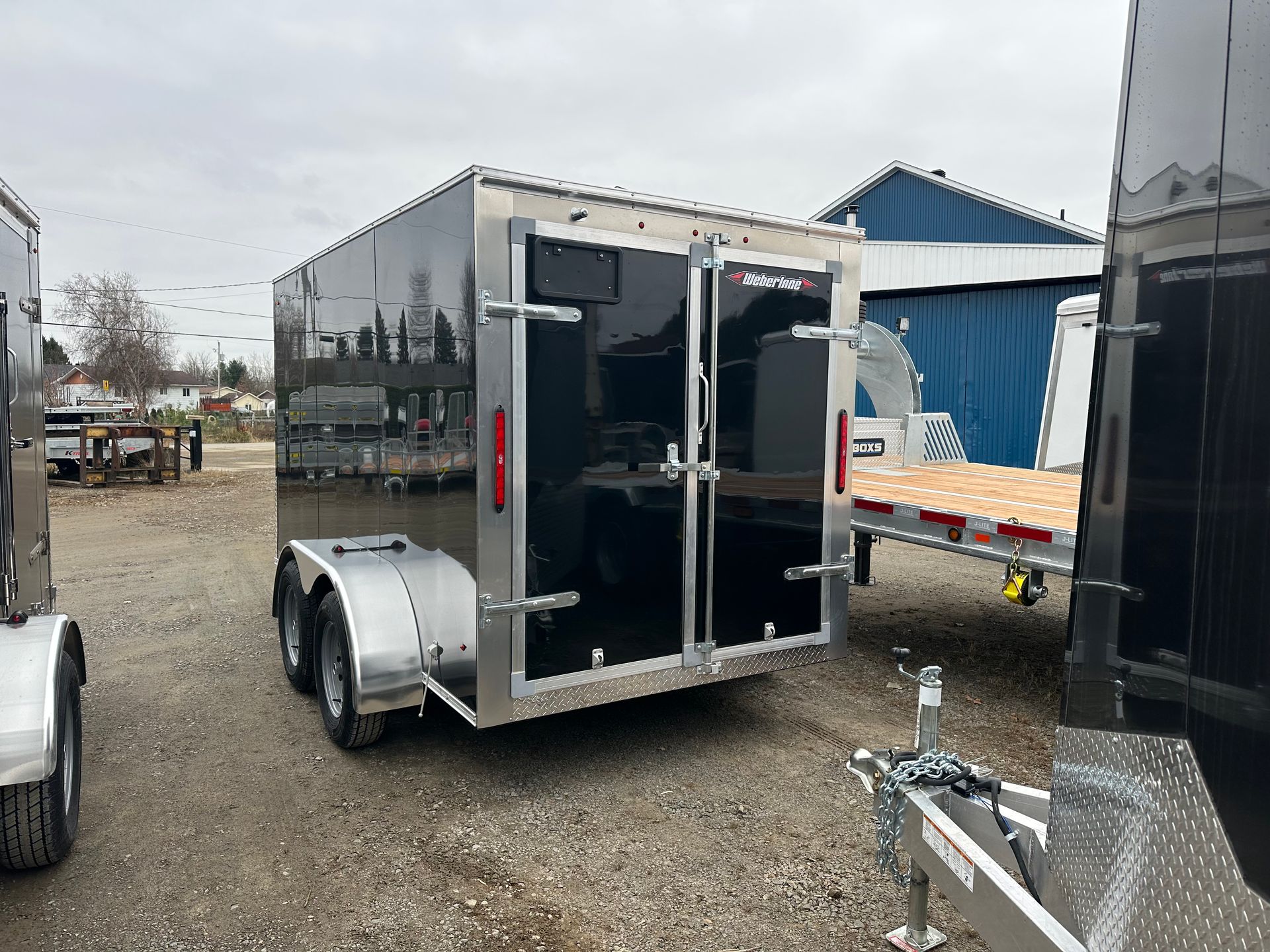 Remorque cargo fermée noire avec des accents argentés, garée à l'extérieur sur du gravier.