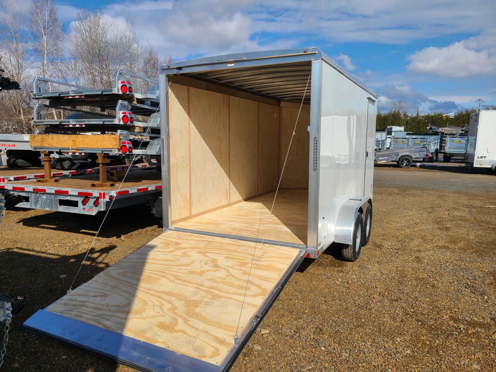 Une remorque blanche avec la porte ouverte est garée sur un terrain en gravier.