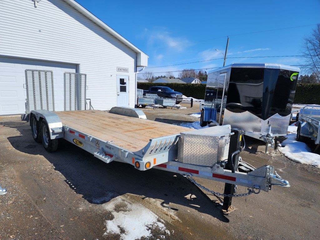 Une remorque à plateau est garée devant un garage.