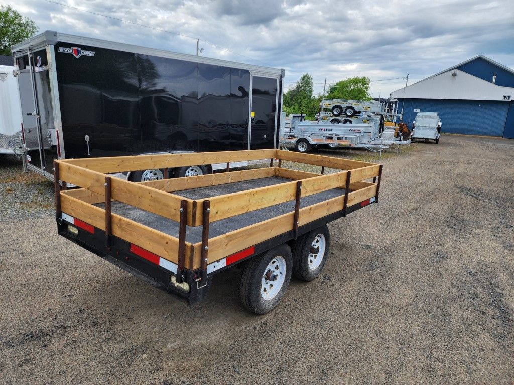 Une remorque avec une terrasse en bois est garée sur un terrain en terre.