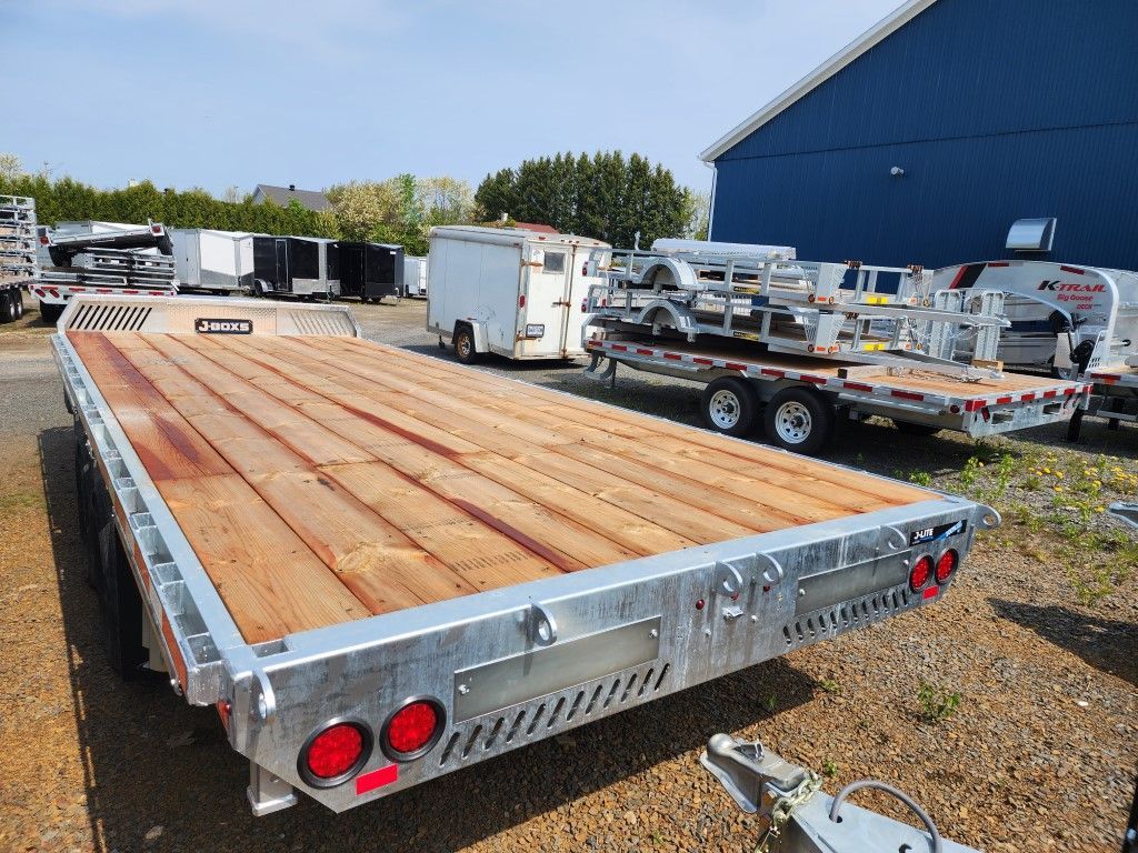 Une remorque avec un pont en bois est garée devant un bâtiment bleu.